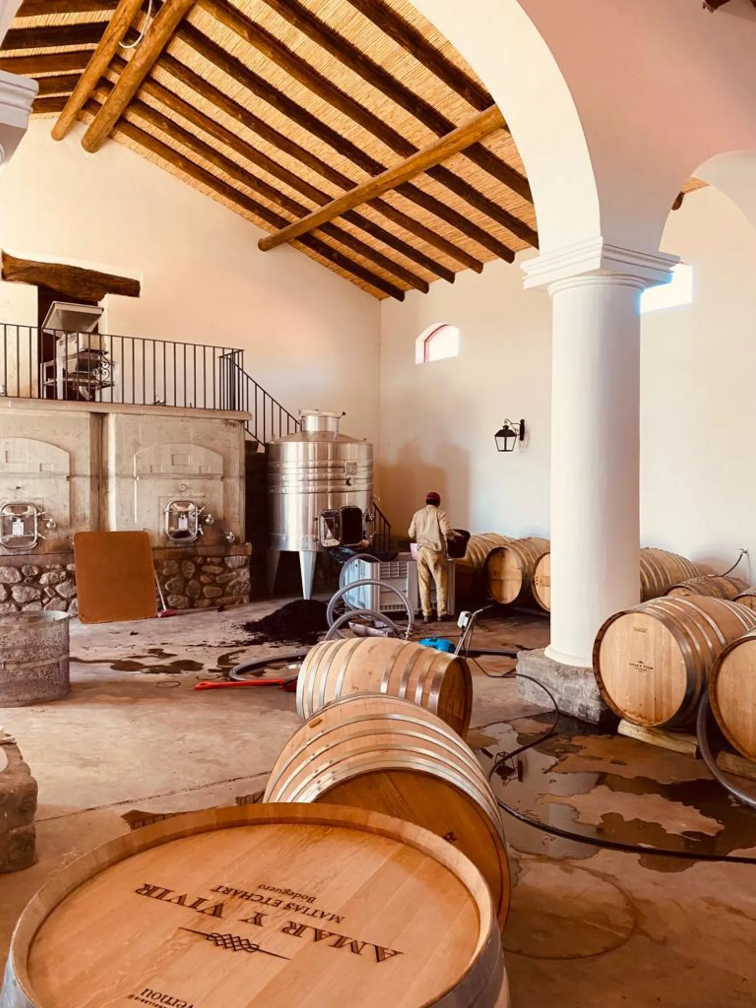 Bodeguero trabajando entre barricas de roble y tanques de acero en la bodega